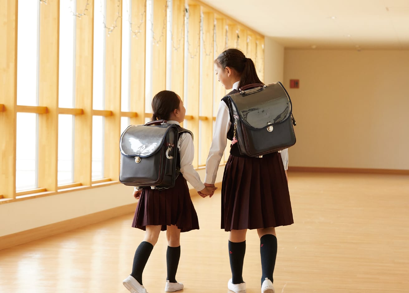 背を向けた上級生と下級生が手を繋いで廊下を歩いている