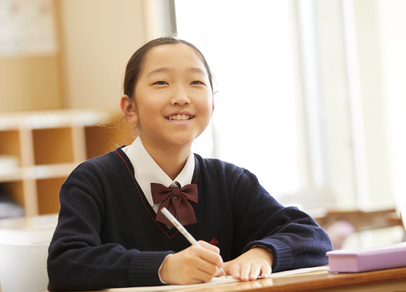 女生徒が机で授業を受けながら、笑顔を向けている